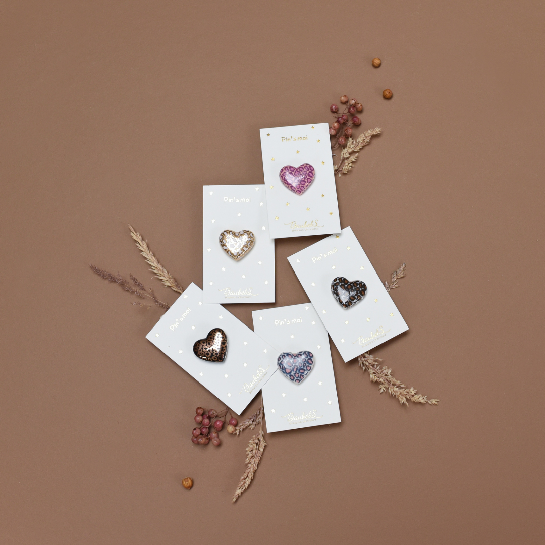 Photo de plusieurs pins ou broches en forme de coeur. Le motif Léopard y est inscrit en plusieurs couleurs, de la marque Baubels