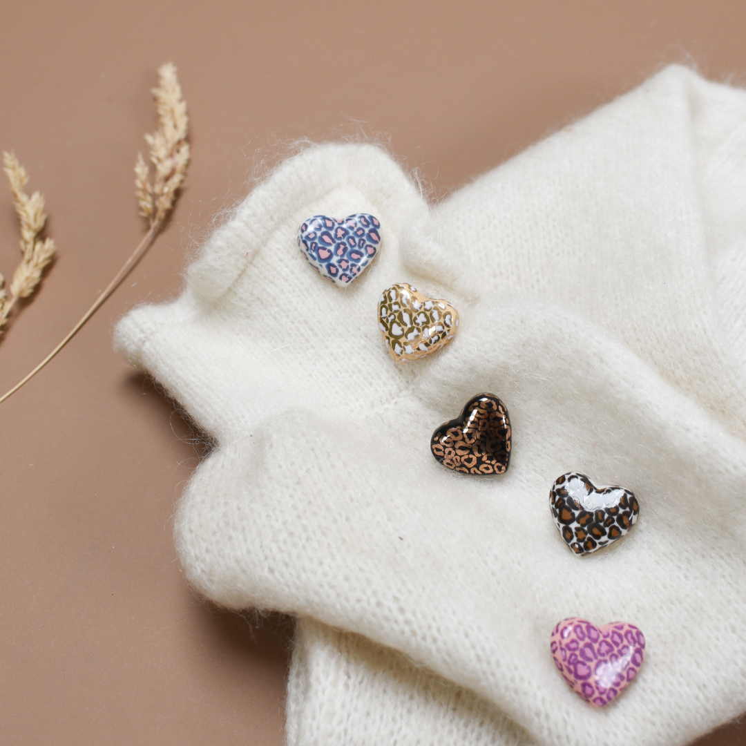 Photo de plusieurs pins ou broches en forme de coeur blanc. Le motif Léopard y est inscrit en plusieurs couleurs, de la marque Baubels