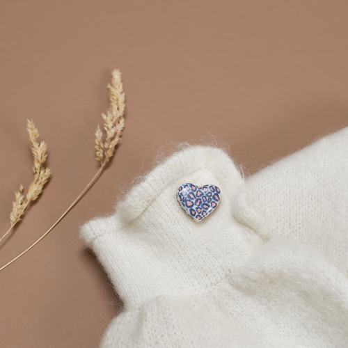 Photo d'un pins ou d'une broche en forme de coeur blanc. Le motif Léopard y est inscrit en couleur bleu et rose, de la marque Baubels