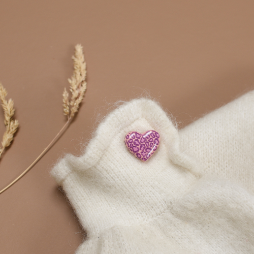 Photo d'un pins ou d'une broche en forme de coeur. Le motif Léopard y est inscrit en couleur violet et rose, de la marque Baubels