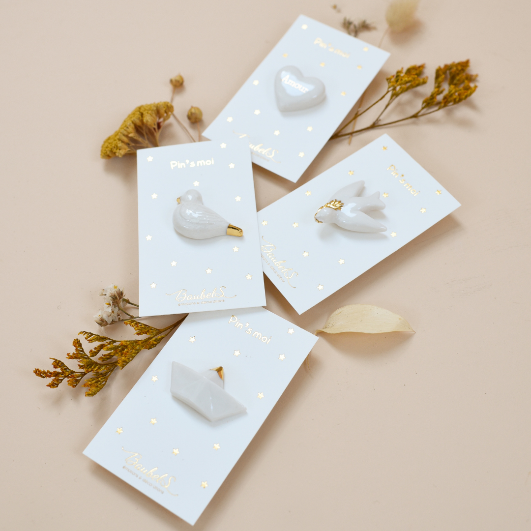 Photo de plusieurs pins ou broches de la collection blanc et doré, de la marque Baubels.