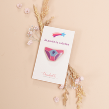 Charger l&#39;image dans la galerie, un pin&#39;s ou une broche en forme de culotte wonderwoman, de couleur rose clair et rose foncé. Celui-ci est accroché sur son support. Un accessoire de mode idéal pour les vêtements ou les sacs à l&#39;occasion des droits de femmes, de la fête des mères ou pour de futurs evjf.
