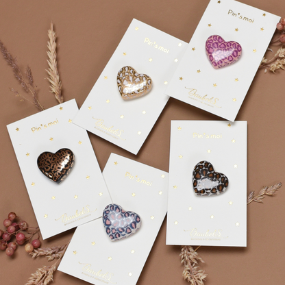 Photo de plusieurs pins ou broches en forme de coeur. Le motif Léopard y est inscrit en plusieurs couleurs, de la marque Baubels